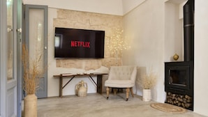 A living room with a stone wall, a flat-screen TV, a fireplace, a chair, and a vase with dried plants. - Trullo dei Noci con Piscina Privata (Ceglie Messapica)