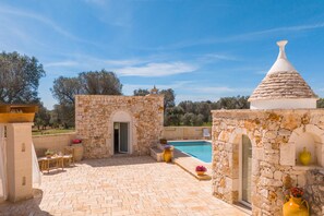 A stone building with a pool, outdoor seating, and a clear blue sky.