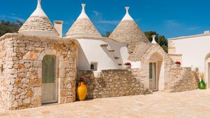 A building with stone walls and white plastered roofs, featuring arched doorways and a tiled courtyard.