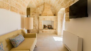 A cozy living room with a stone fireplace, a sofa with patterned cushions, and a flat-screen TV mounted on the wall.