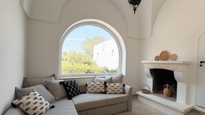 A cozy room with a large arched window, a fireplace with decorative items, and a beige sofa with patterned cushions. - Villa Vittoria in Ostuni (Ostuni)