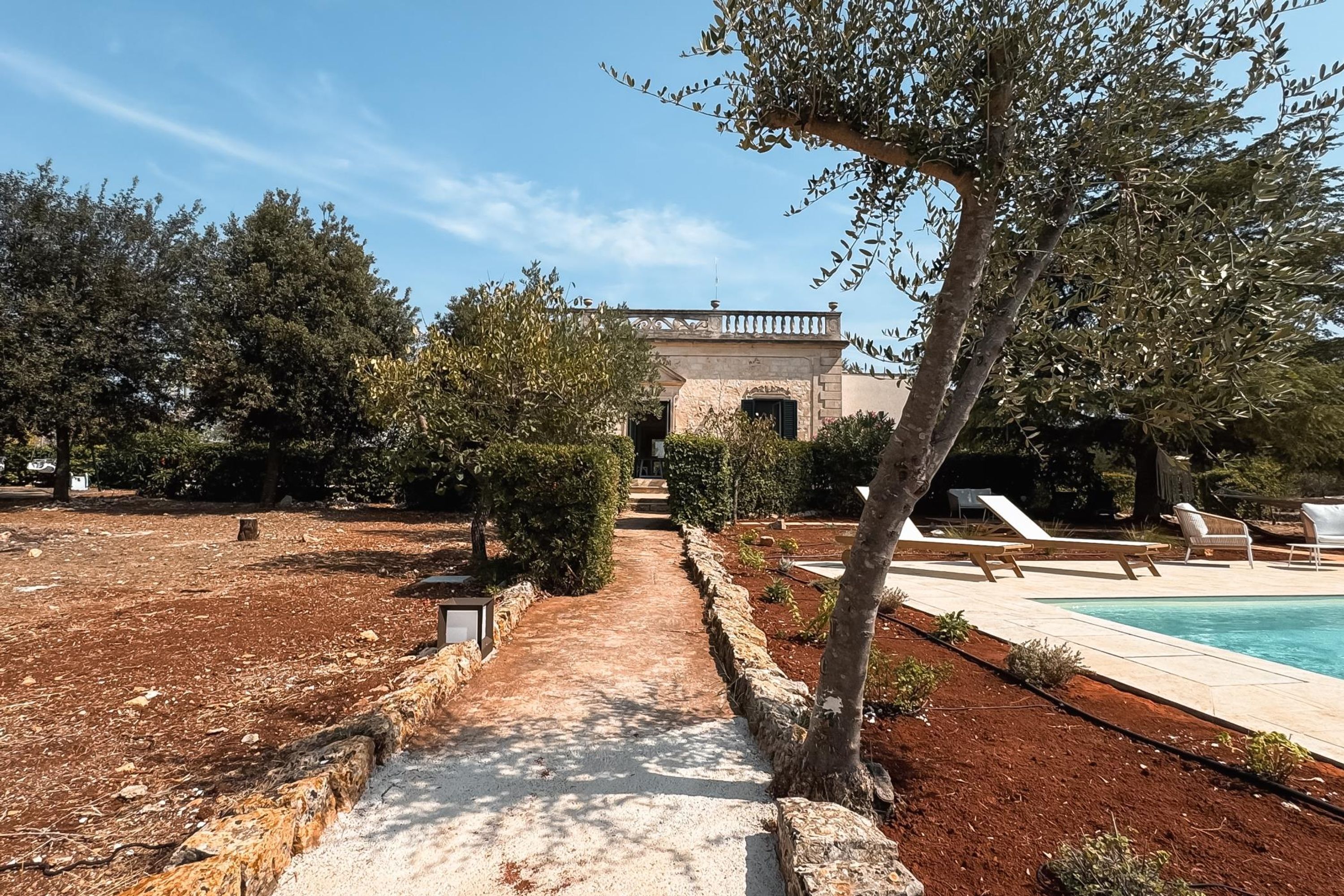 A pool area with lounge chairs, a stone pathway, and a building with an arched entrance.