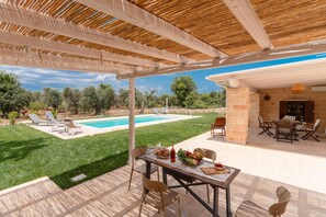 A covered outdoor patio with a pool, seating, and a stone wall. - Trullo Tramonto in SAN Michele Salentino (San Michele Salentino)