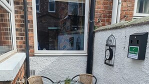 A small patio with a round table and four wicker chairs, a clock on the wall, and a sign indicating a smoking area. - Chic & Modern Escape (Salford)