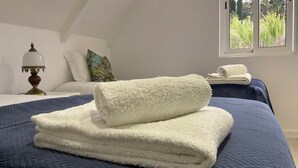 Una cama bien hecha con un edredón azul y dos toallas blancas dobladas.