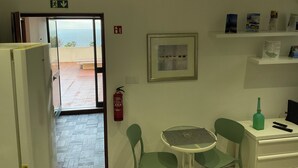 Una habitación con vista al mar, un extintor, un cuadro enmarcado y una estantería con objetos.