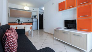 A modern living room with a sofa, a television, and orange cabinets. - Relaxing Apartment With Terrace and Pool in Bibione (San Michele al Tagliamento)