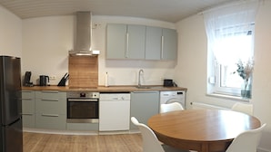 A compact kitchen with a stove, oven, dishwasher, and a dining area with a table and chairs. - Your vacation home (Andernach)
