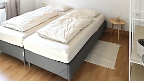 A bedroom with two beds, a wooden floor, a white ceiling, and a small bedside table with a lamp. - Your vacation home (Andernach)