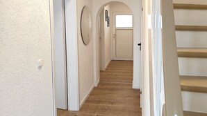 A hallway with wooden flooring, white walls, and a staircase with a beige handrail. - Your vacation home (Andernach)