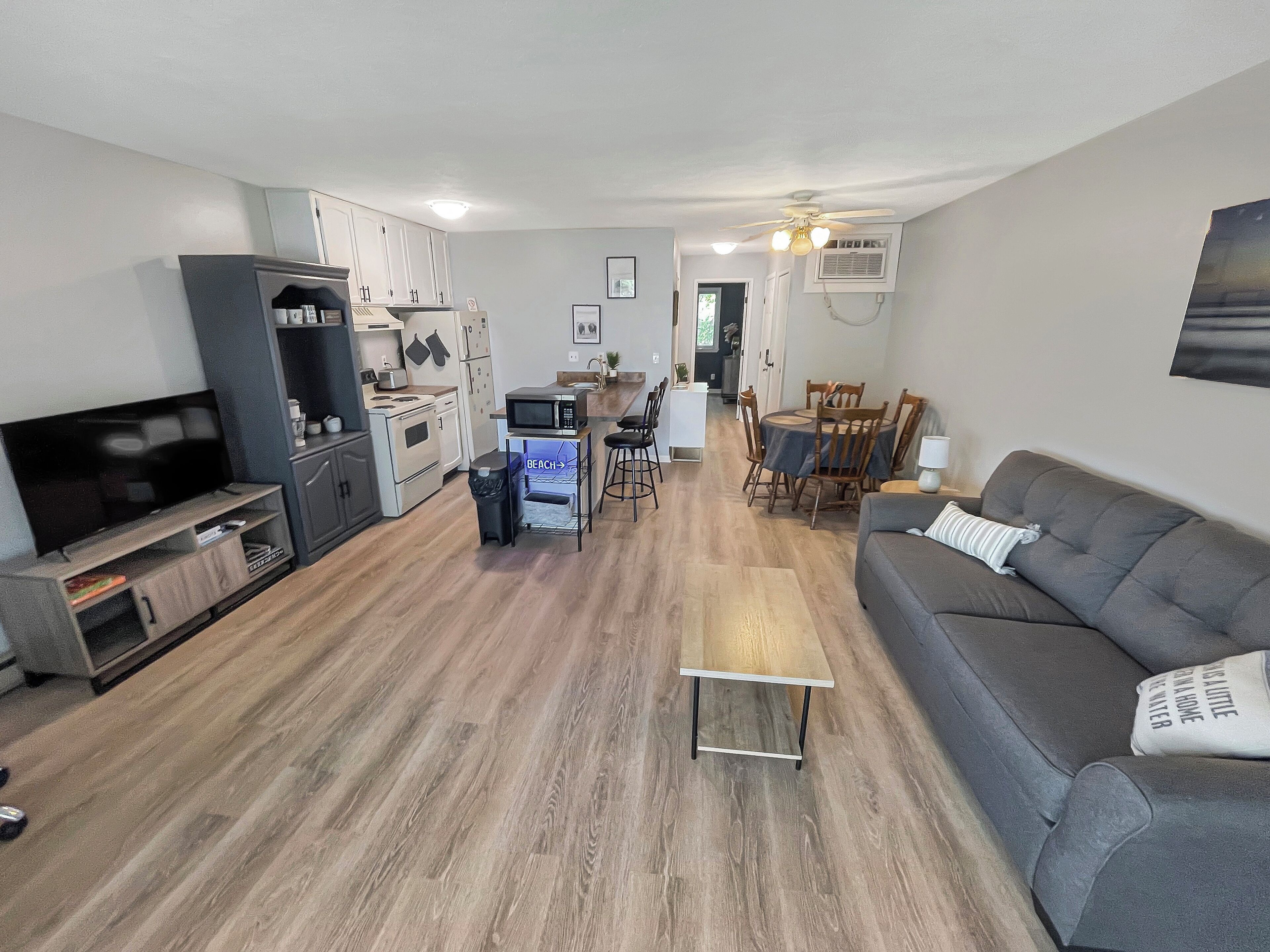 A modern living room with a grey sofa, a flat-screen TV, and a dining area with wooden chairs and a table.