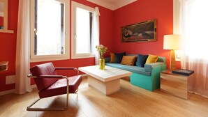 A modern living room with a red wall, a blue sofa, a red chair, and a wooden coffee table.
