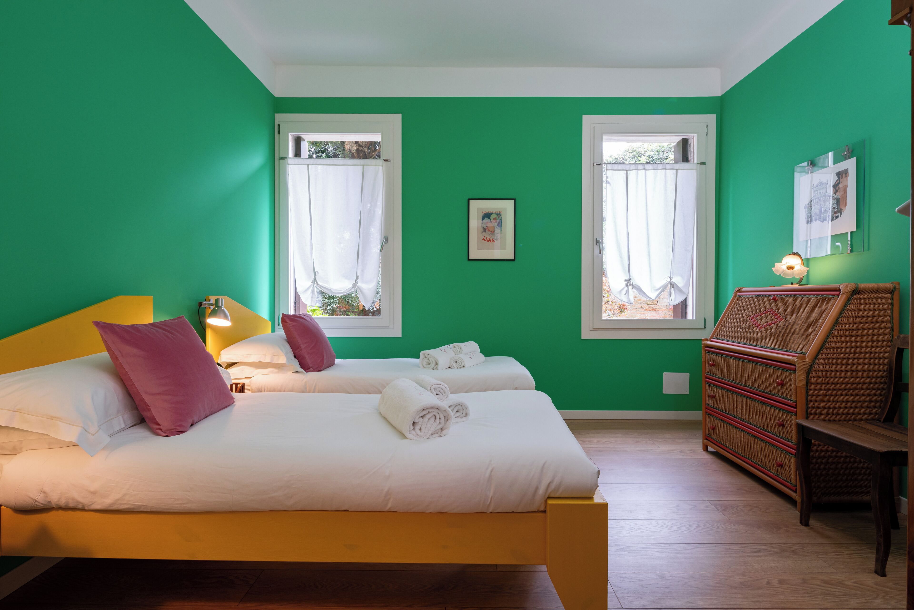 Una habitación con dos camas, un aparador de madera y una silla de mimbre.