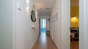A hallway with wooden flooring, white walls, and a door leading to a kitchen area.