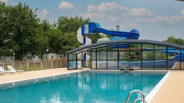 A swimming pool with a water slide, lounge chairs, and a glass-enclosed area.