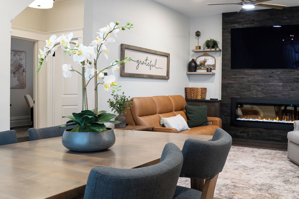 Un salon moderne avec une cheminée, un coin repas avec une grande table et des chaises, et un canapé agrémenté d’un coussin vert.