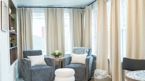 Un coin salon confortable avec deux fauteuils gris, une petite table ronde et un pouf blanc.
