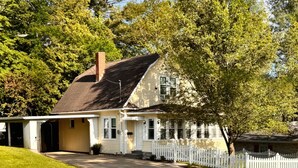 Une maison de plain-pied avec un porche à l’avant, une clôture en bois peinte en blanc et une pelouse bien entretenue.