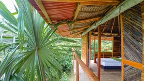 A wooden structure with a thatched roof, a wooden deck, and a bed with a white sheet.