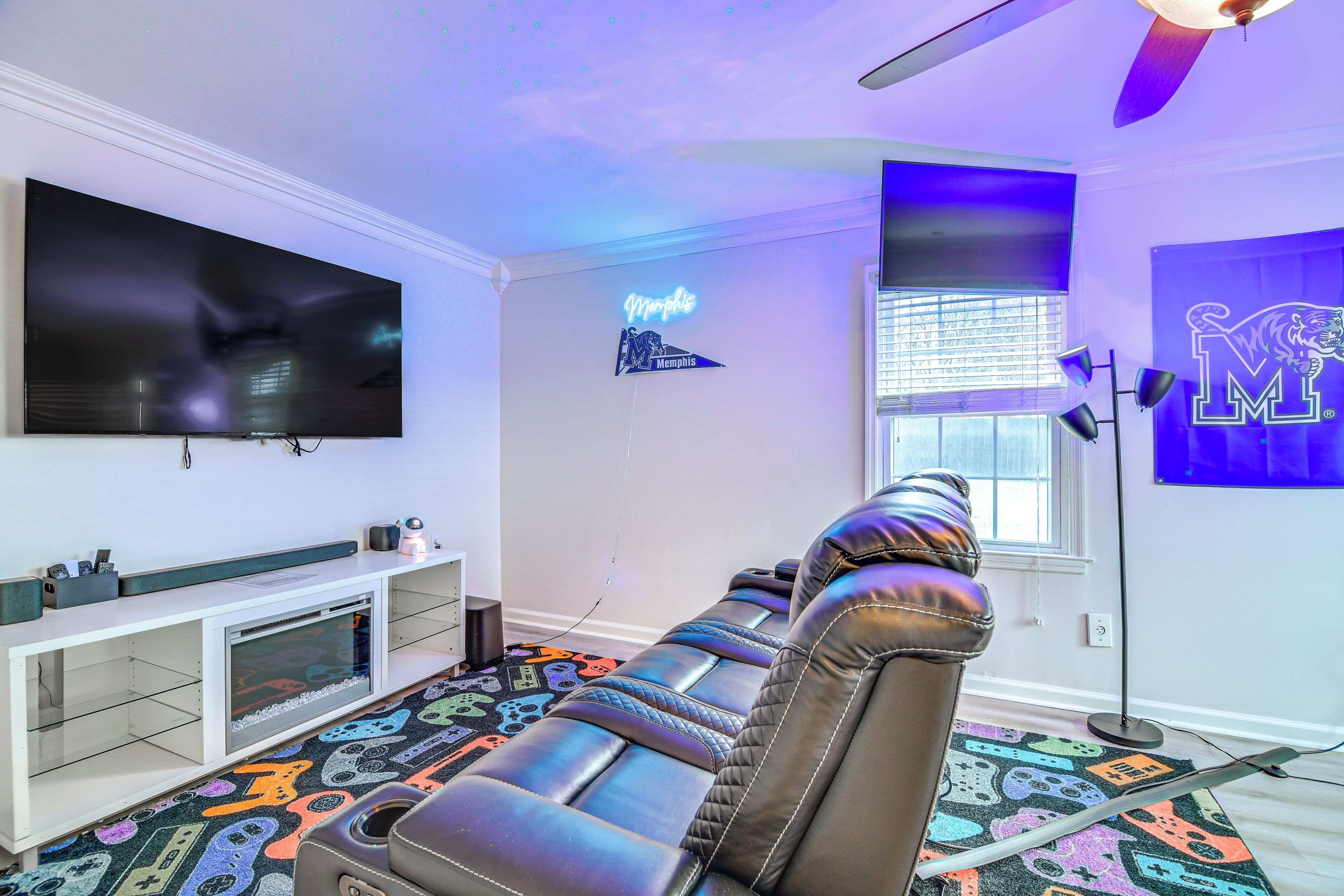 A modern living room with a large flat-screen TV, a neon sign, and a leather sofa.