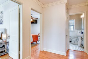 Un pasillo con una cama, un baño con lavamanos y una puerta que da a otra habitación.