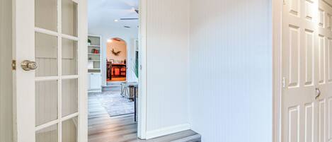 A hallway with a wooden floor, white walls, and a door with a glass panel.