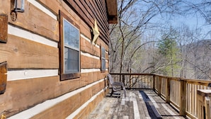 Una cabaña de madera con terraza y ventanas que dan a un bosque.