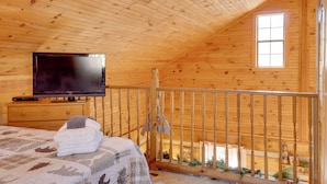 Habitación tipo cabaña de madera con una cama, un televisor y un balcón con barandilla.