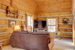 L’intérieur d’un chalet confortable, avec des murs en bois, un canapé en cuir marron, un téléviseur et un fauteuil à bascule.