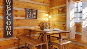 Interior de una cabaña de madera con un letrero que dice 'BIENVENIDOS', una mesa con bancos, un centro de mesa floral y un letrero que dice 'Animales del Bosque'.