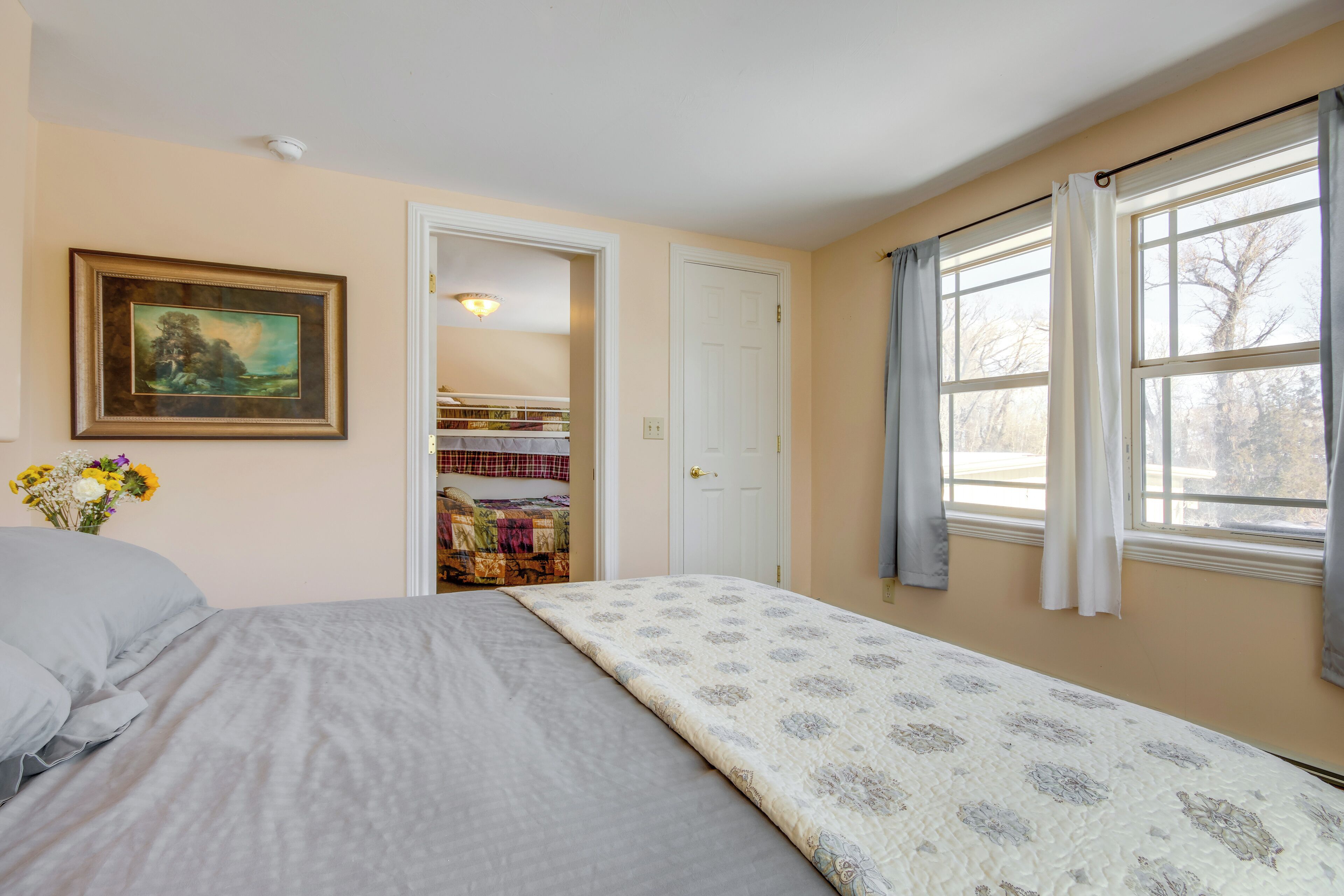A bedroom with a bed, a door leading to a closet, a window with curtains, and a painting on the wall.