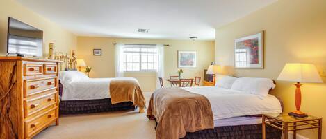 A hotel room with two beds, a wooden dresser, a television, a desk with a lamp, and a window with curtains.