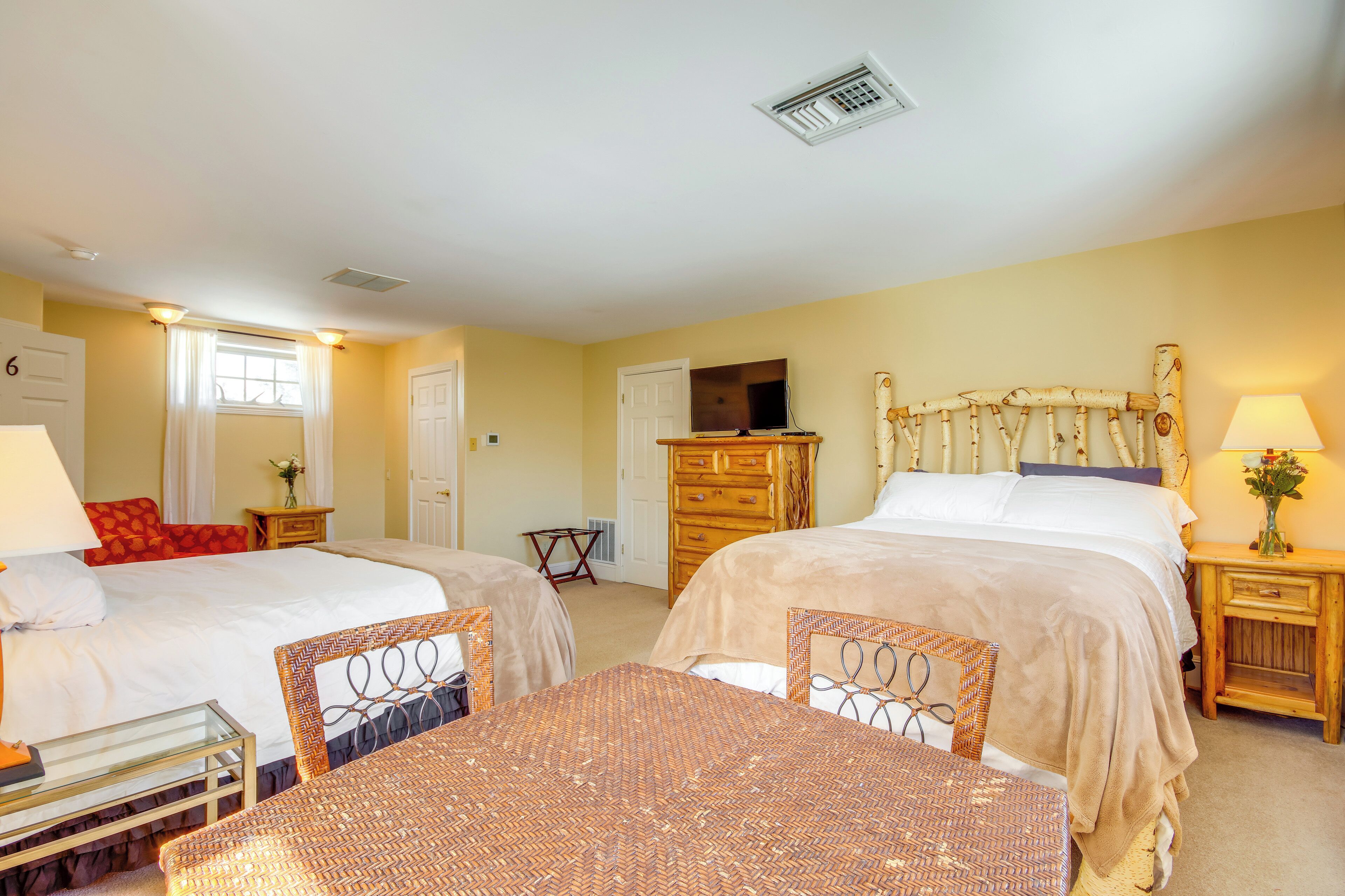 A hotel room with two beds, a TV, a wooden headboard, a table, and a lamp.