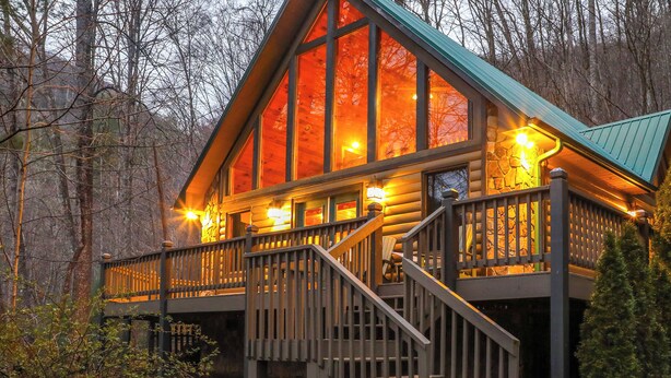 Une cabane en rondins dotée d’un balcon et d’un escalier, entourée d’arbres.