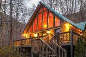 A log cabin with a balcony and stairs, surrounded by trees.