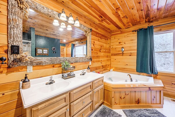 A wooden cabin bathroom with a large mirror, two sinks, a bathtub, and a window with a curtain.