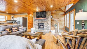 L’intérieur chaleureux d’un chalet avec une cheminée en pierre, un plafond en bois et un espace de vie comprenant un canapé et une table basse.