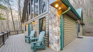 Une cabane en rondins avec une terrasse, deux fauteuils Adirondack et un mur en pierre.