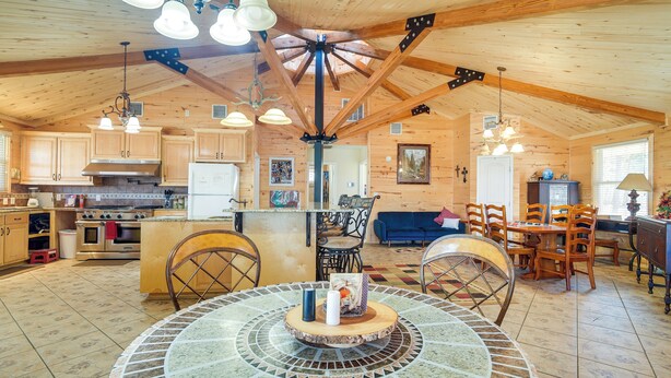 A spacious kitchen with wooden cabinets, a central island, and a dining area with chairs and a table. - Fire Pit, Views: Lakefront Toledo Bend Retreat! (Many)