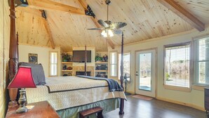 A bedroom with a wooden ceiling, a bed with a quilt, a nightstand, a red lamp, a wooden bench, a ceiling fan, and a window with blinds. - Fire Pit, Views: Lakefront Toledo Bend Retreat! (Many)