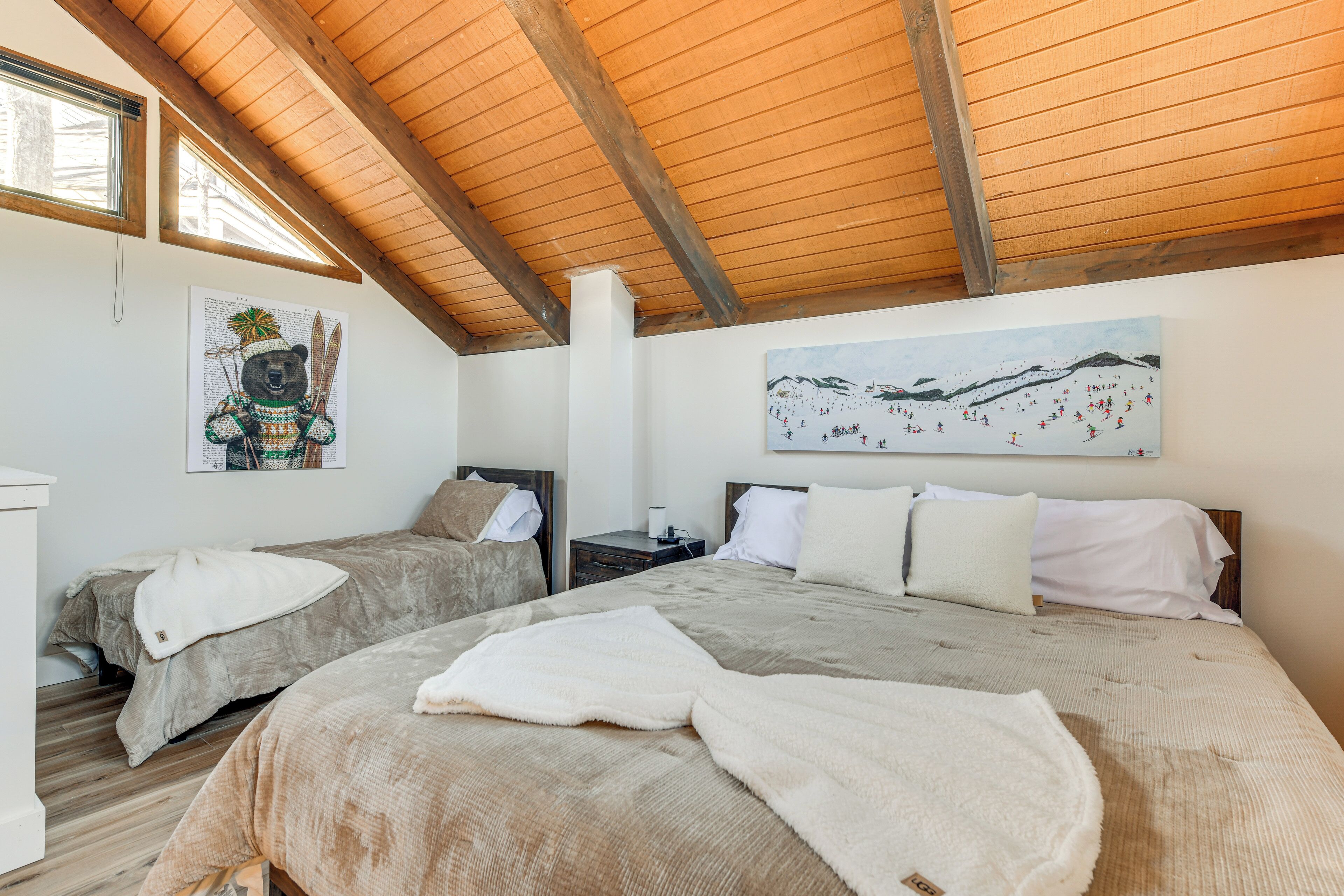 Ein Schlafzimmer mit zwei Betten, Holzbalkendecke, einem Bärenbild und einer Berglandschaft.