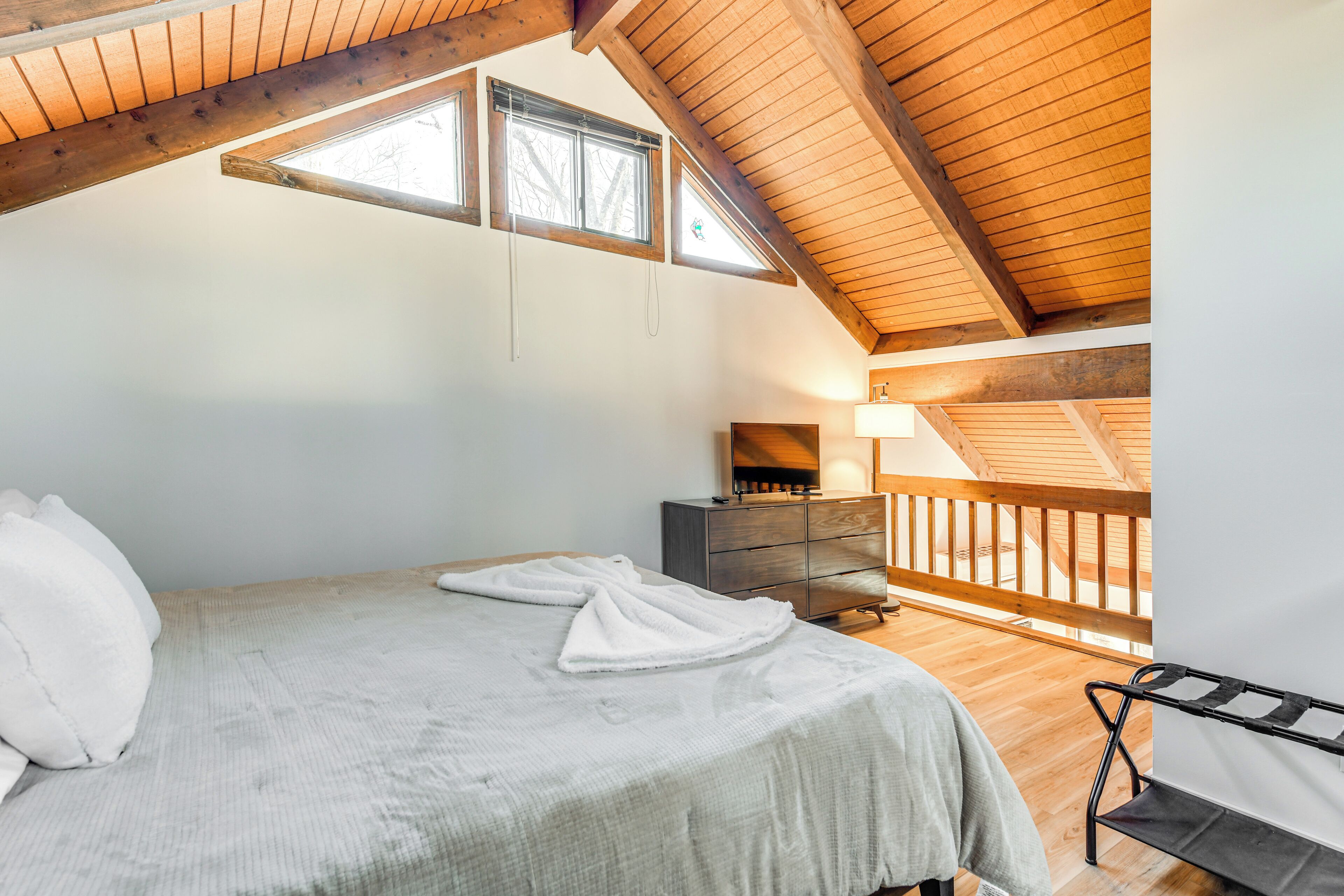 A bedroom with a sloped ceiling, a bed with white linens, a dresser, and a bench.