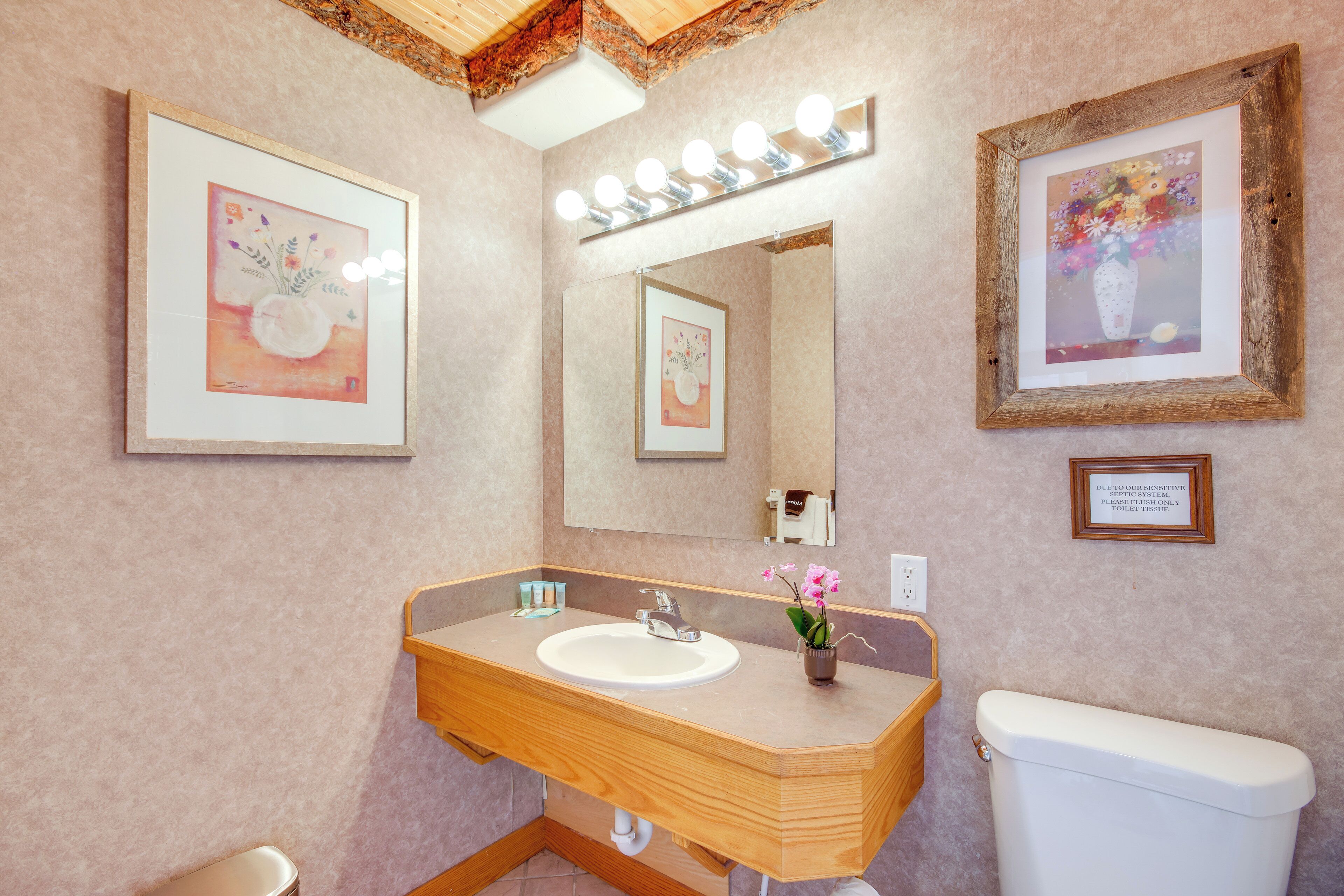 A modern bathroom with a wooden vanity, a large mirror, and framed artwork on the walls.