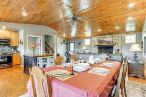 Un comedor con techo de madera, chimenea de piedra y cocina al fondo.