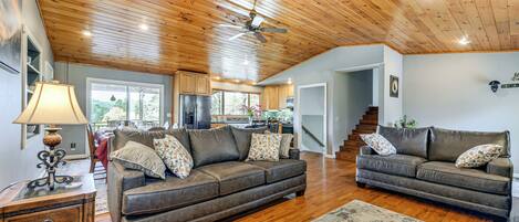 A spacious living room with a wooden ceiling, two sofas with decorative pillows, a side table, and a lamp.