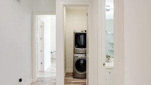 Une buanderie équipée d’un lave-linge et d’un sèche-linge superposés, avec un plancher en bois et un mur blanc.