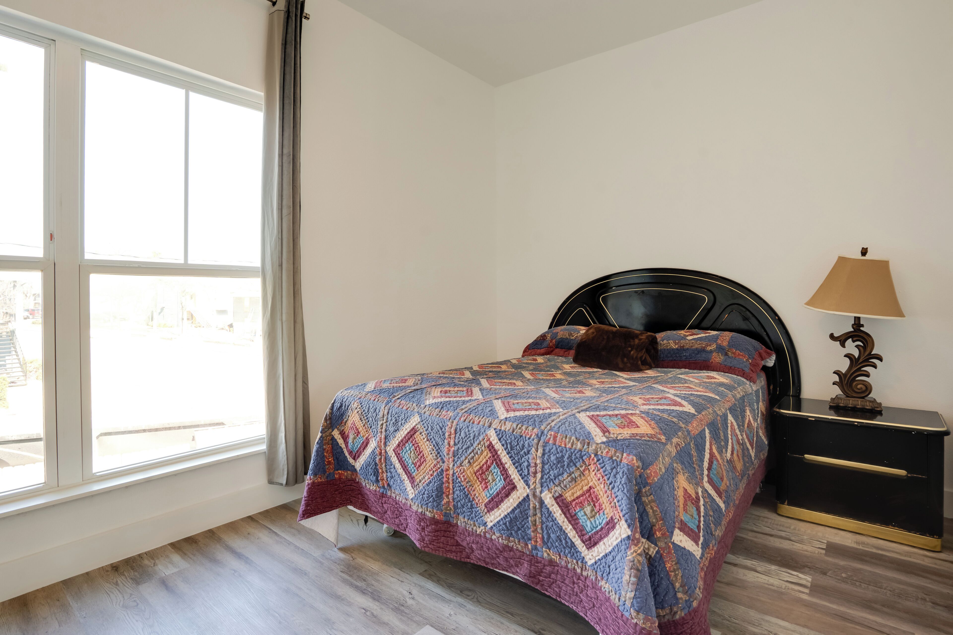 Une chambre à coucher avec un lit, une table de chevet, une lampe et une fenêtre avec des rideaux.