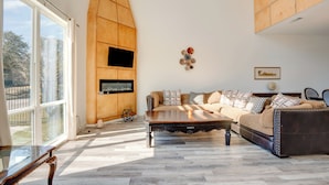 Un salon spacieux doté d’une grande fenêtre, d’un mur d’accent en bois, d’un ensemble de canapés et d’une table basse.