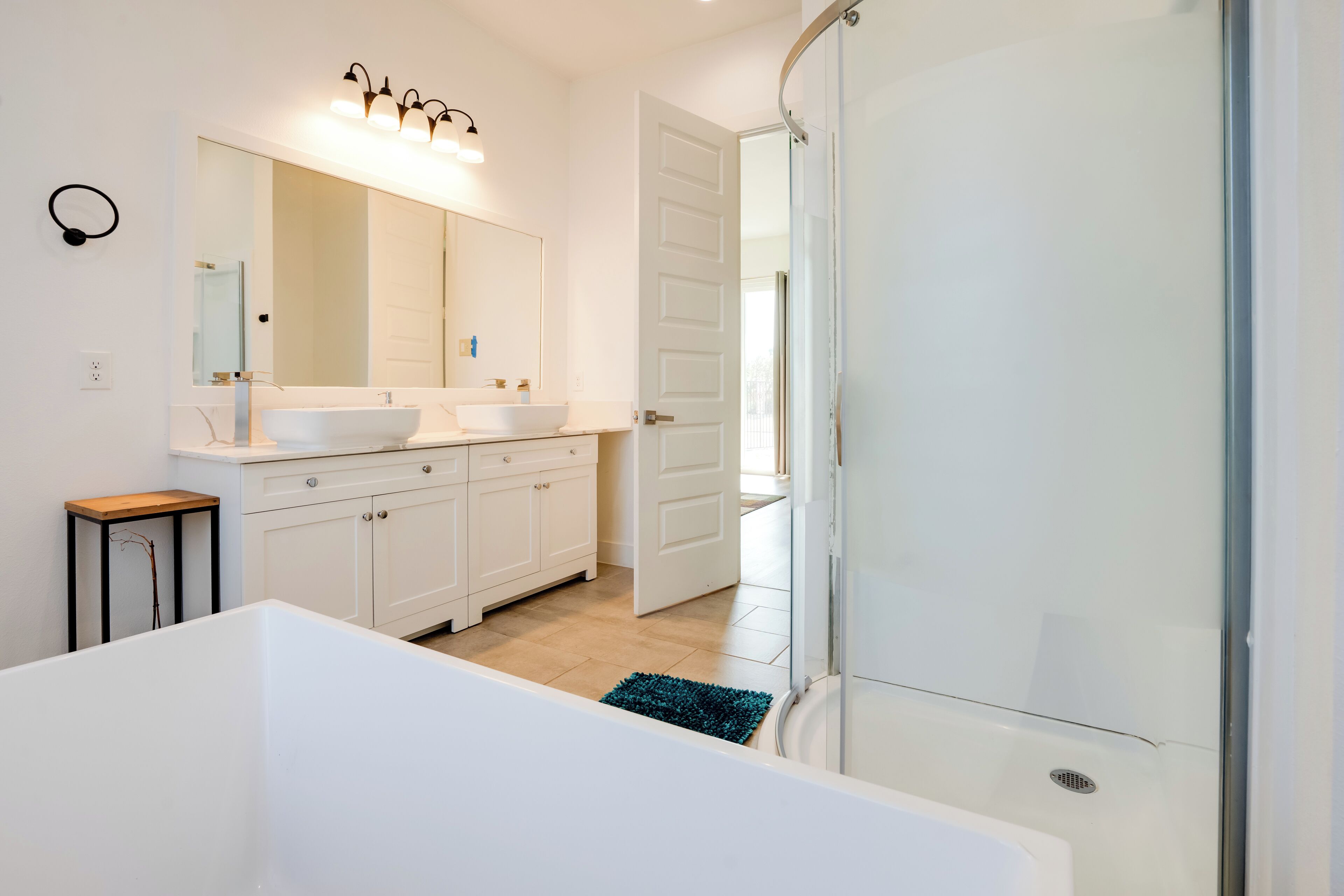 A modern bathroom with a bathtub, two sinks, a large mirror, and a shower.