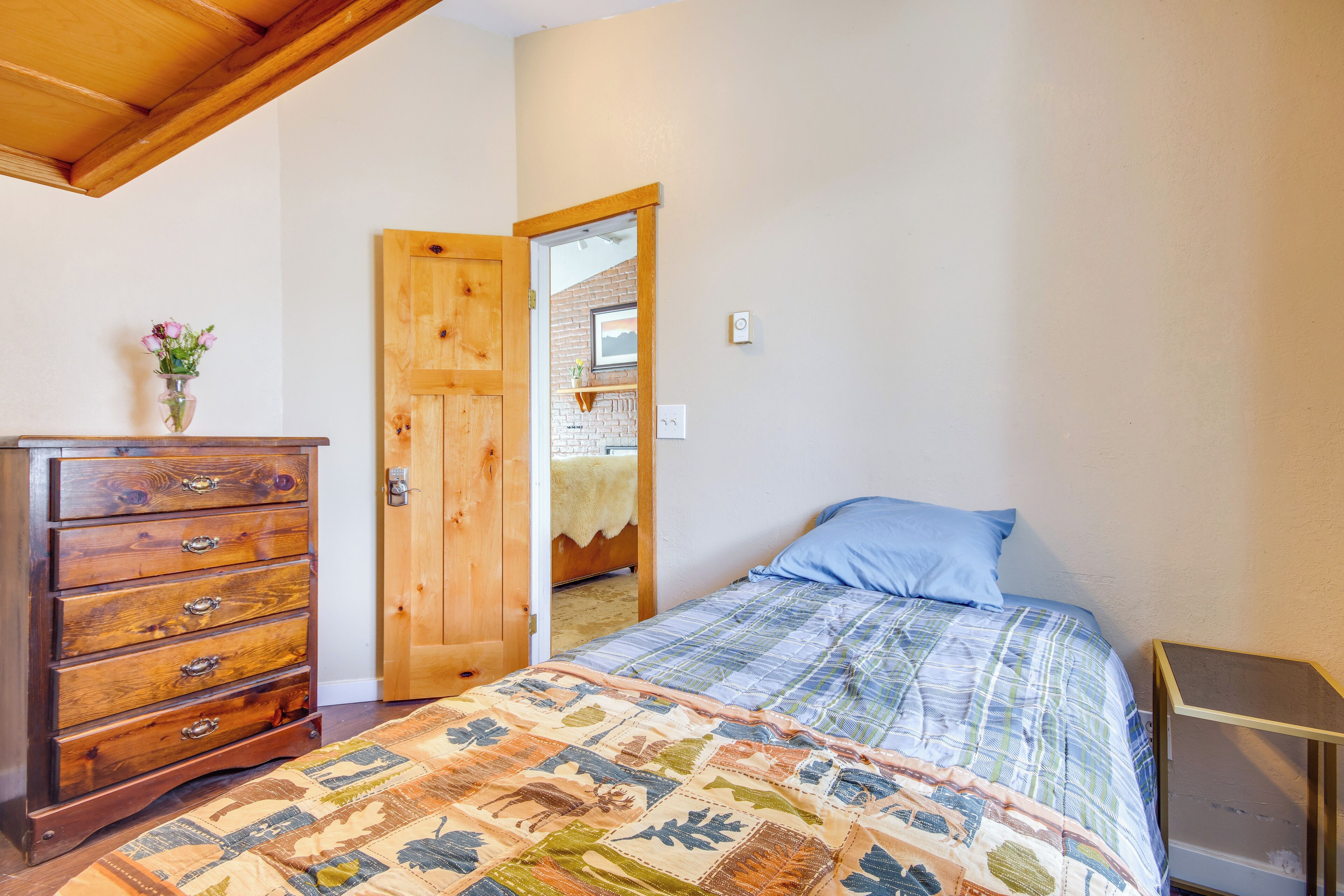 A bedroom with a wooden dresser, a quilted bedspread, and a wooden door leading to another room.